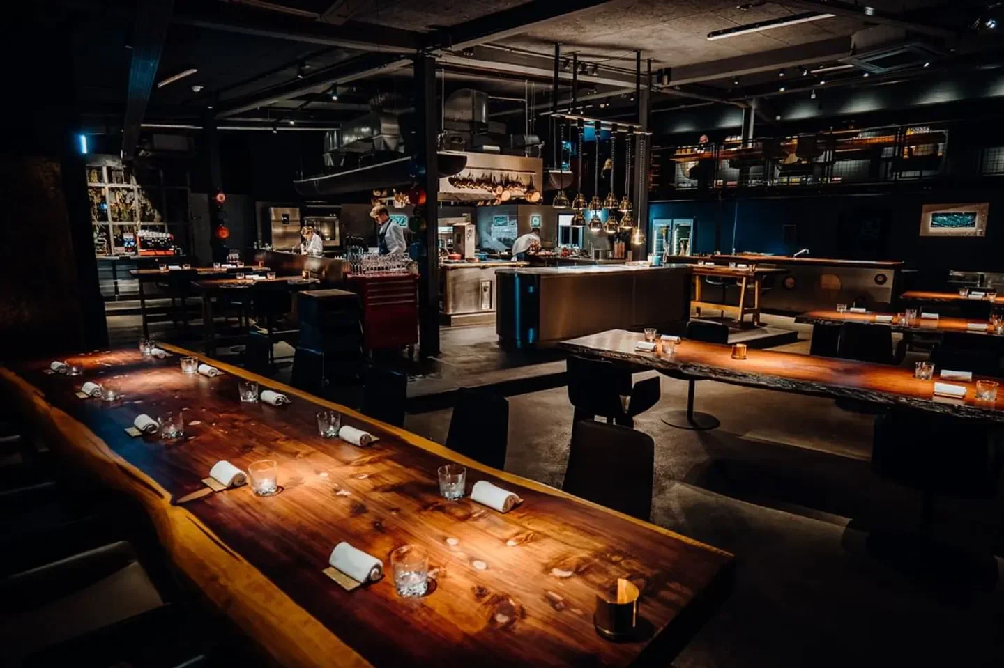 Elegant dining interior at 100/200 Kitchen, Hamburg, with long wooden tables and open kitchen.