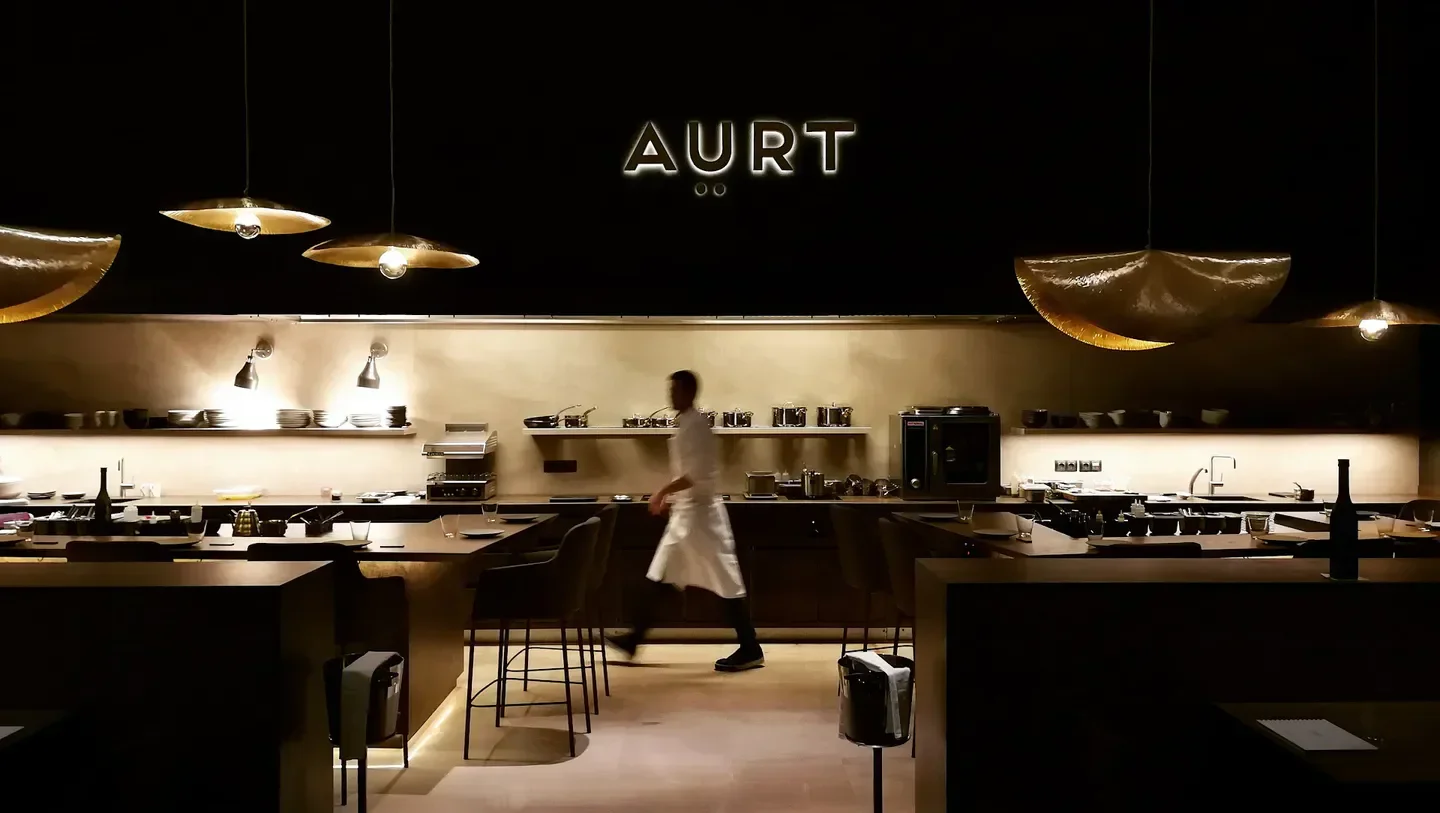 Interior view of Aürt restaurant in Barcelona, with ambient lighting and a chef working.