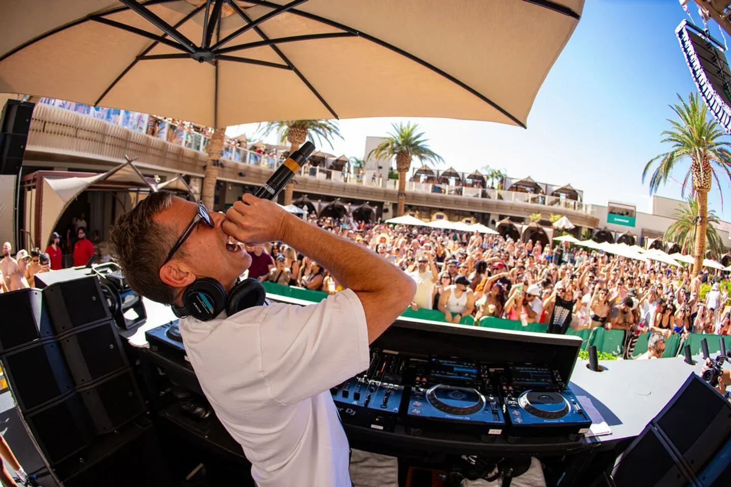 DJ performs for a large crowd at Ayu Dayclub in Las Vegas under a bright sunny sky.