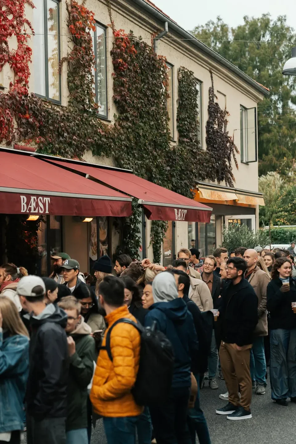 Busy crowd outside Bæst restaurant in Copenhagen, red awning and building facade.