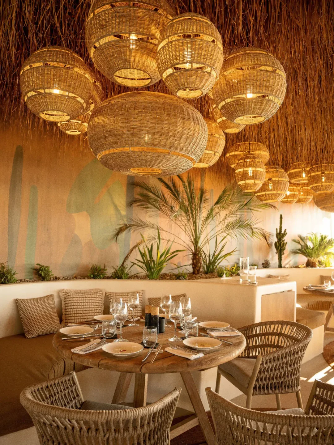 Woven pendant lights and palm trees in the tropical interior of Beefbar Santorini restaurant.