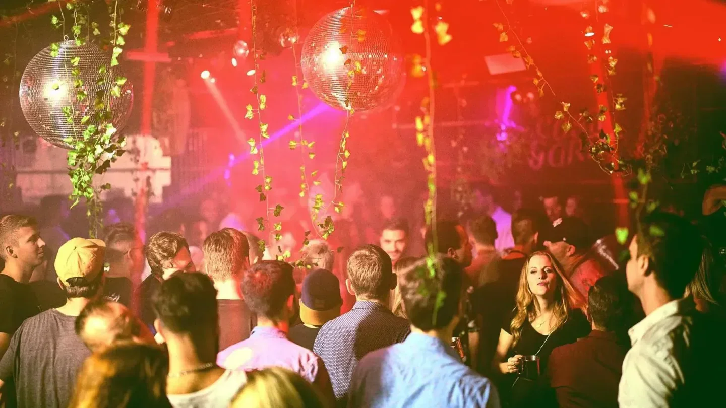 Energetic crowd at Bellevue nightclub in Zurich, with disco ball and ivy decor.