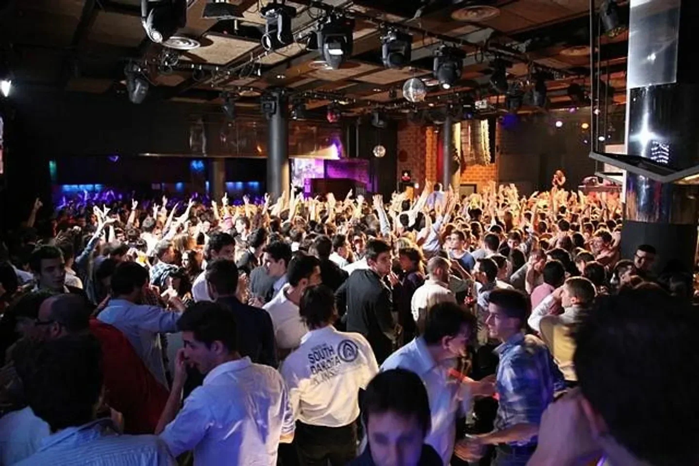 Energetic crowd partying inside Bikini Club in Barcelona, hands in the air, nightlife.