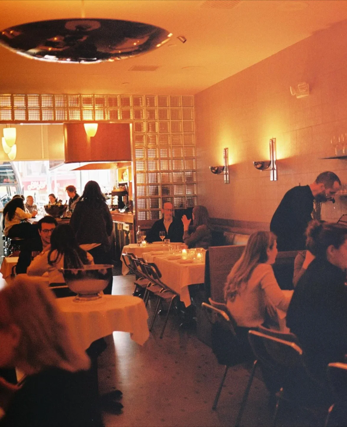 Warmly lit interior of Bridges restaurant, featuring glass block walls and elegant dining tables for a cozy city dining experience.