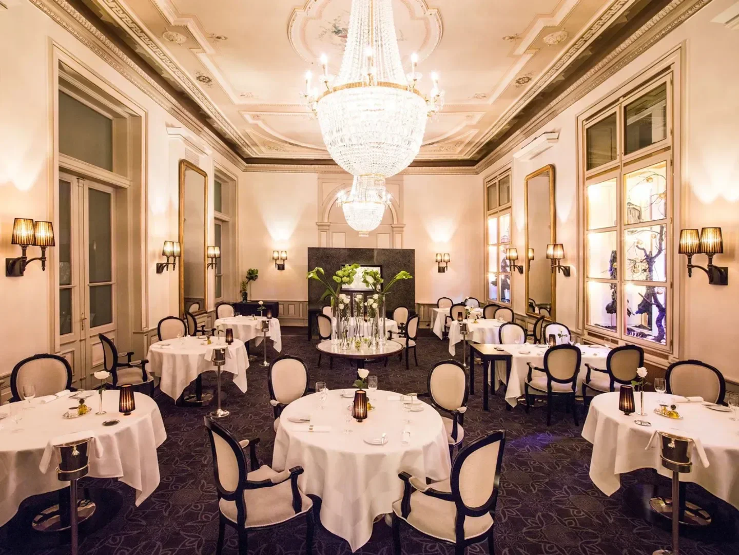 Elegant dining room at Ca d'Oro restaurant in St. Moritz with chandeliers and white tablecloths.