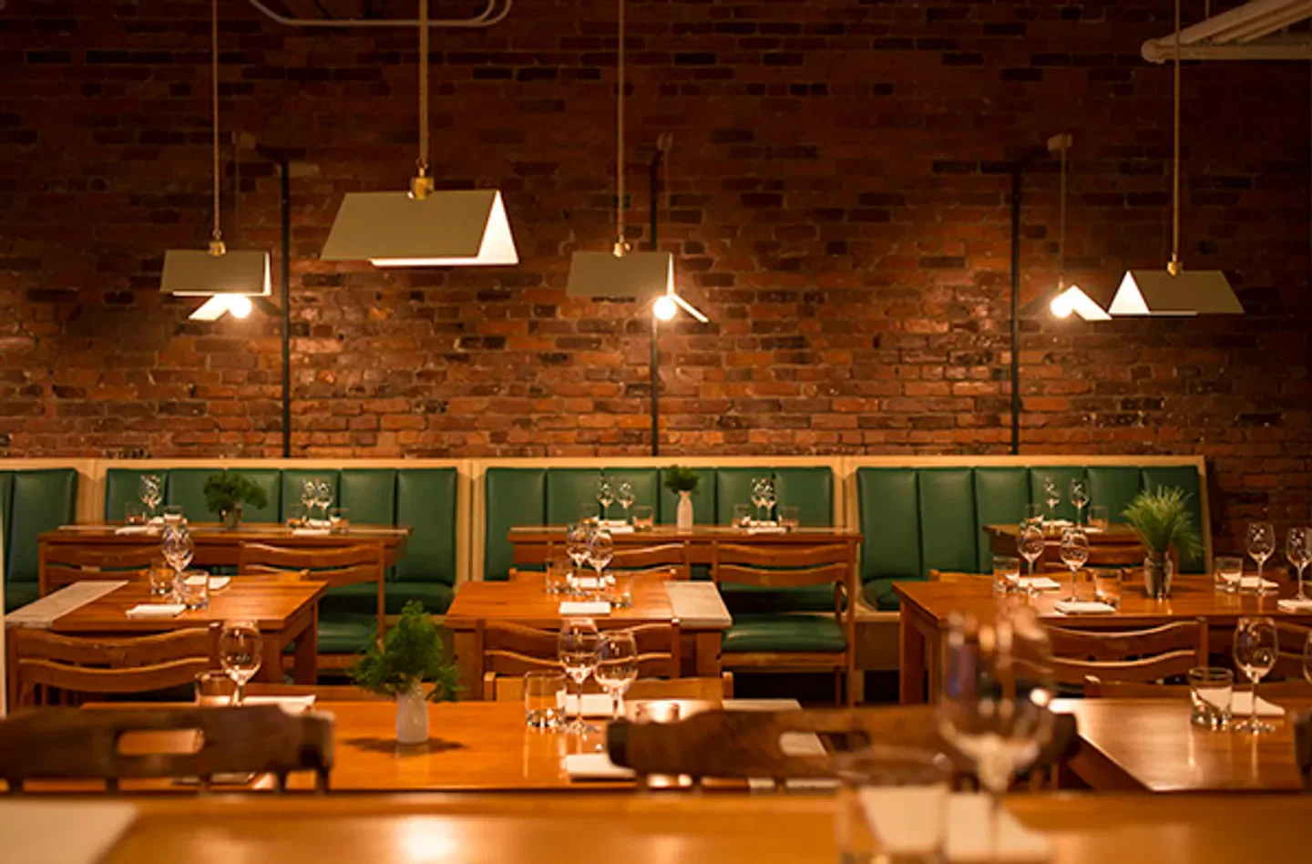 Candide restaurant in Montreal, featuring wooden tables, green booths, and brick walls.