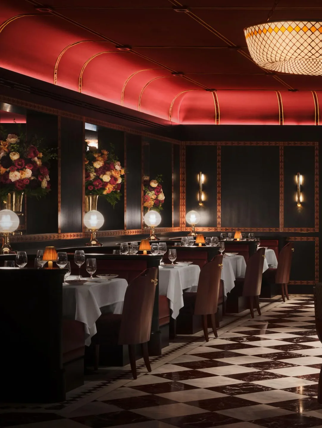 Luxurious dining room at Carbone restaurant in the city featuring red curved ceilings, checkered floors, and floral arrangements.