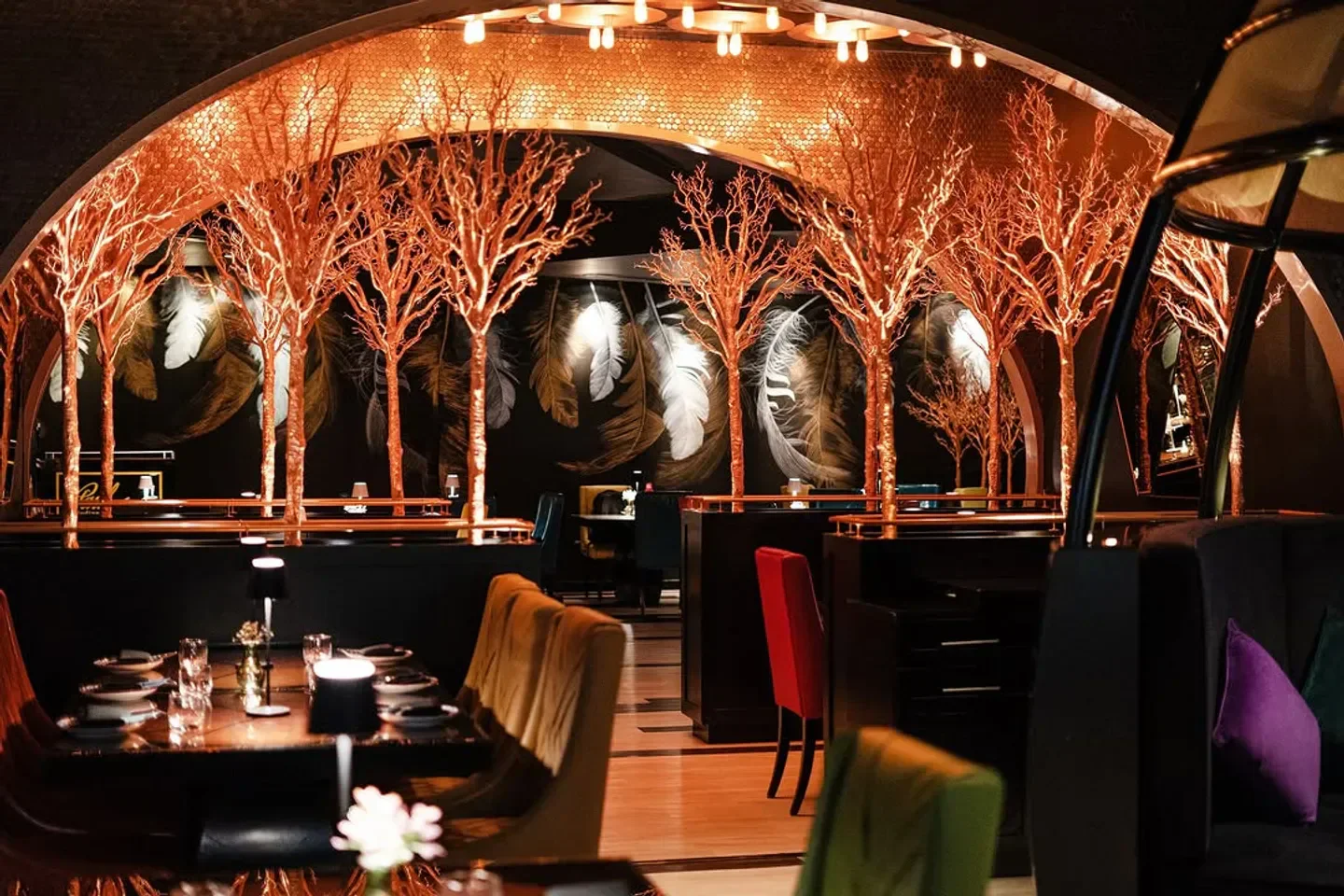 Elegant dining interior at Carnival Dubai, featuring unique golden tree decor and feather art.