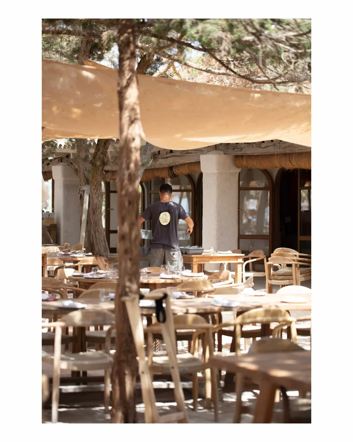 Casa Jondal Ibiza beach club outdoor dining area with wooden tables and chairs under a canopy.