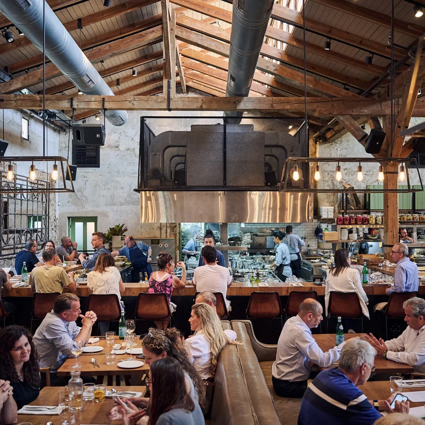 Inside Claro restaurant in Tel Aviv, with patrons dining and a view of the kitchen.