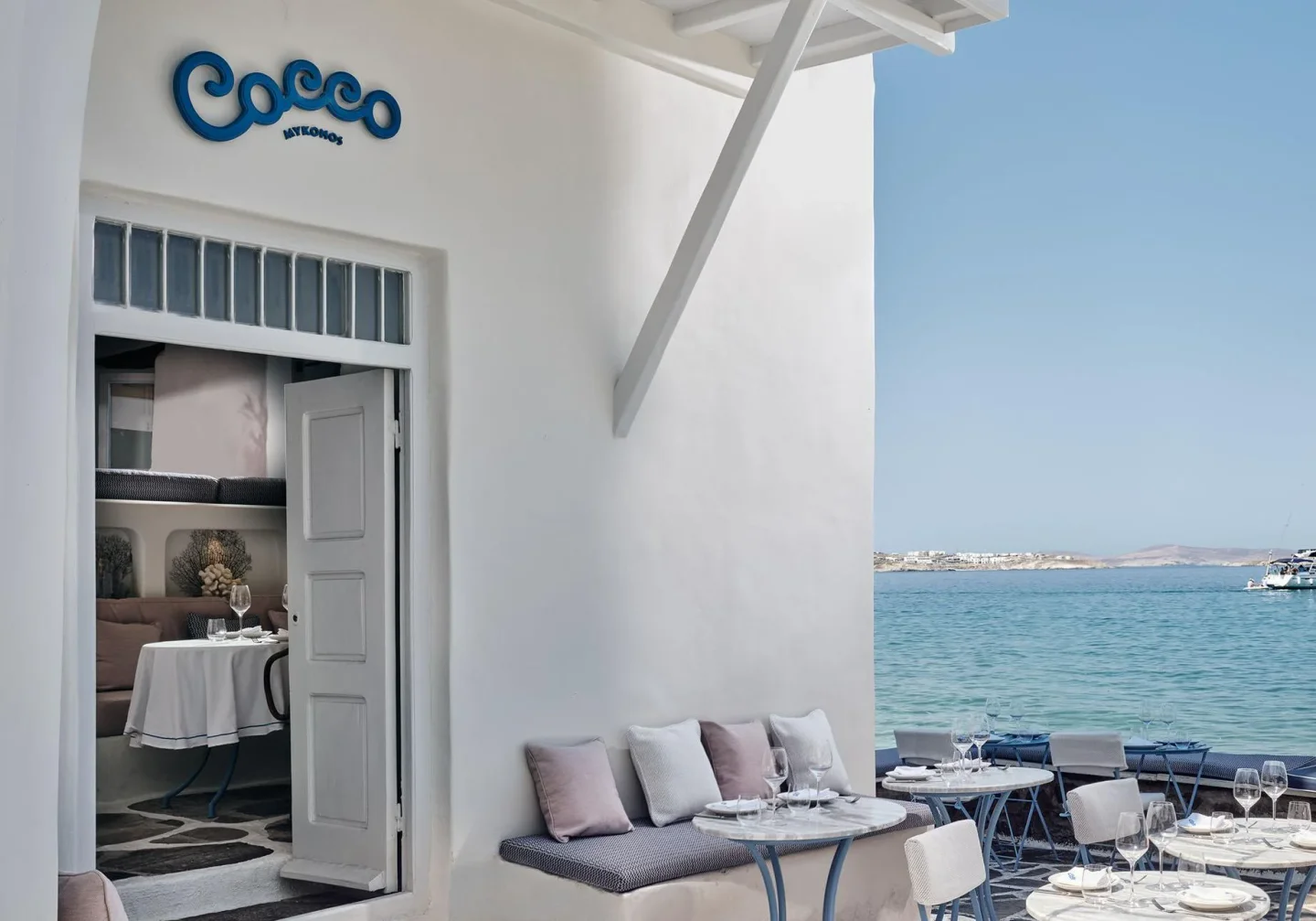 Cocco Mykonos restaurant outdoor seating with tables set by the blue Aegean Sea.