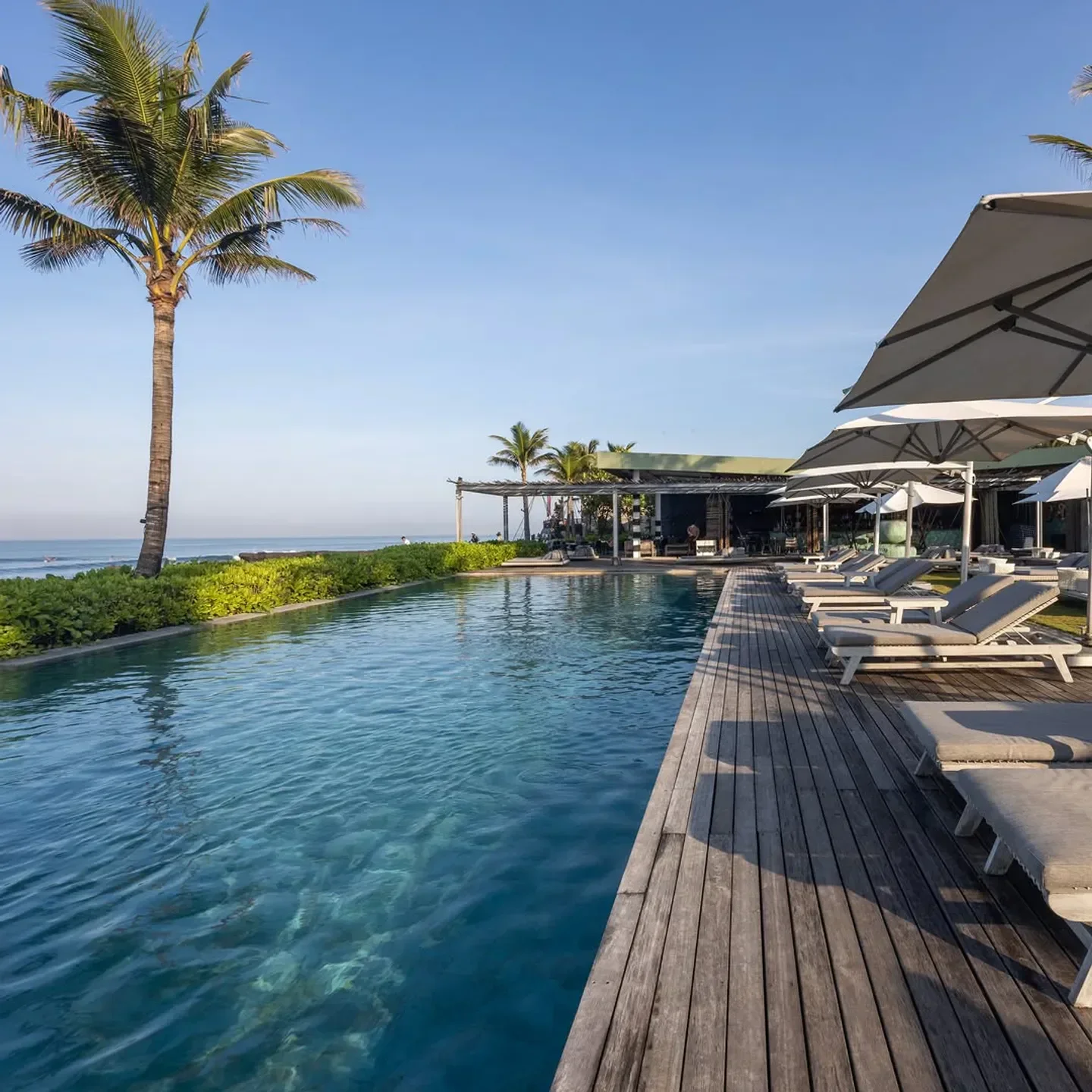 Poolside view at COMO Beach Club in Bali, offering sunbeds and palm trees