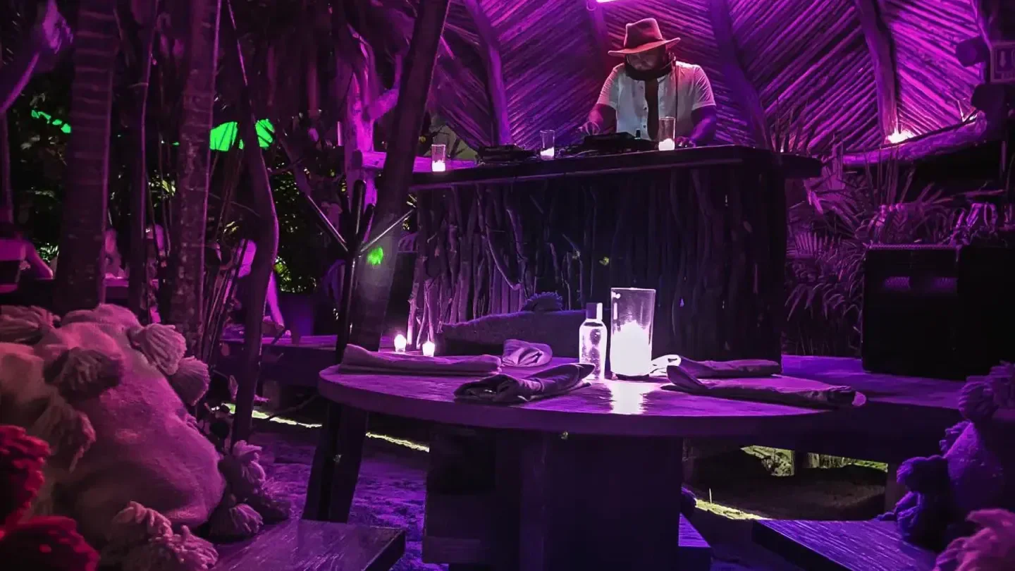 DJ playing at Confessions nightclub in Tulum, surrounded by lush, purple-lit tropical decor