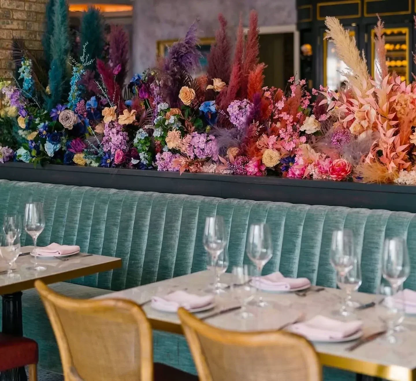 Coquette Boston restaurant interior with floral decor, tables set, and a cozy teal booth.