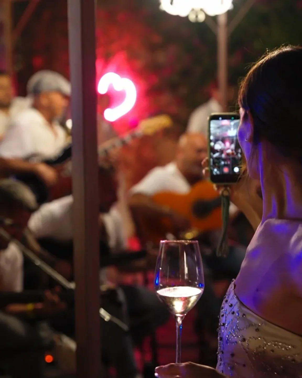 Woman filming live music performance at CUE restaurant in Porto Cervo with a glass of wine.