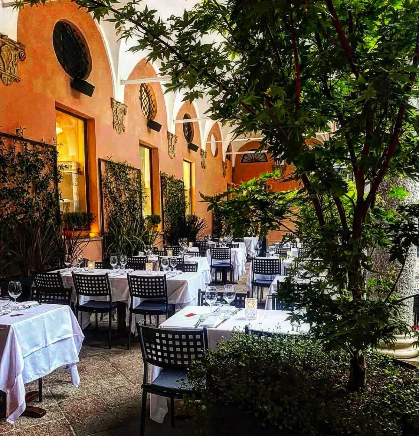 Outdoor dining at Dal Bolognese in Rome with tables set among trees and arches.