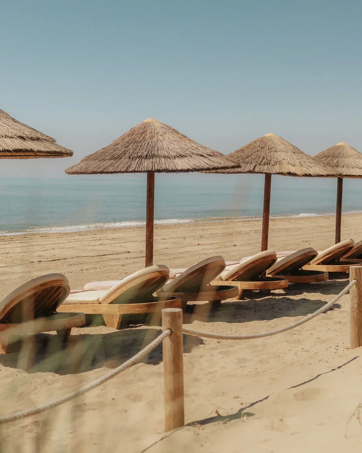 Dune Beach Marbella: empty lounge chairs and thatched umbrellas on sandy beach with ocean view.