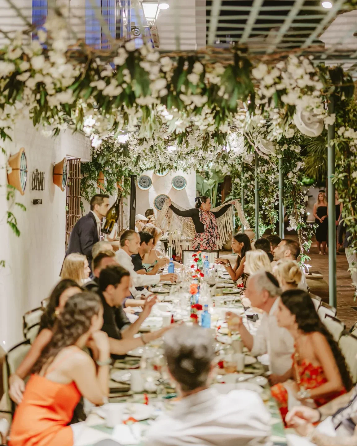 Diners enjoy a vibrant flamenco performance at El Pimpi restaurant in Marbella under floral canopy.