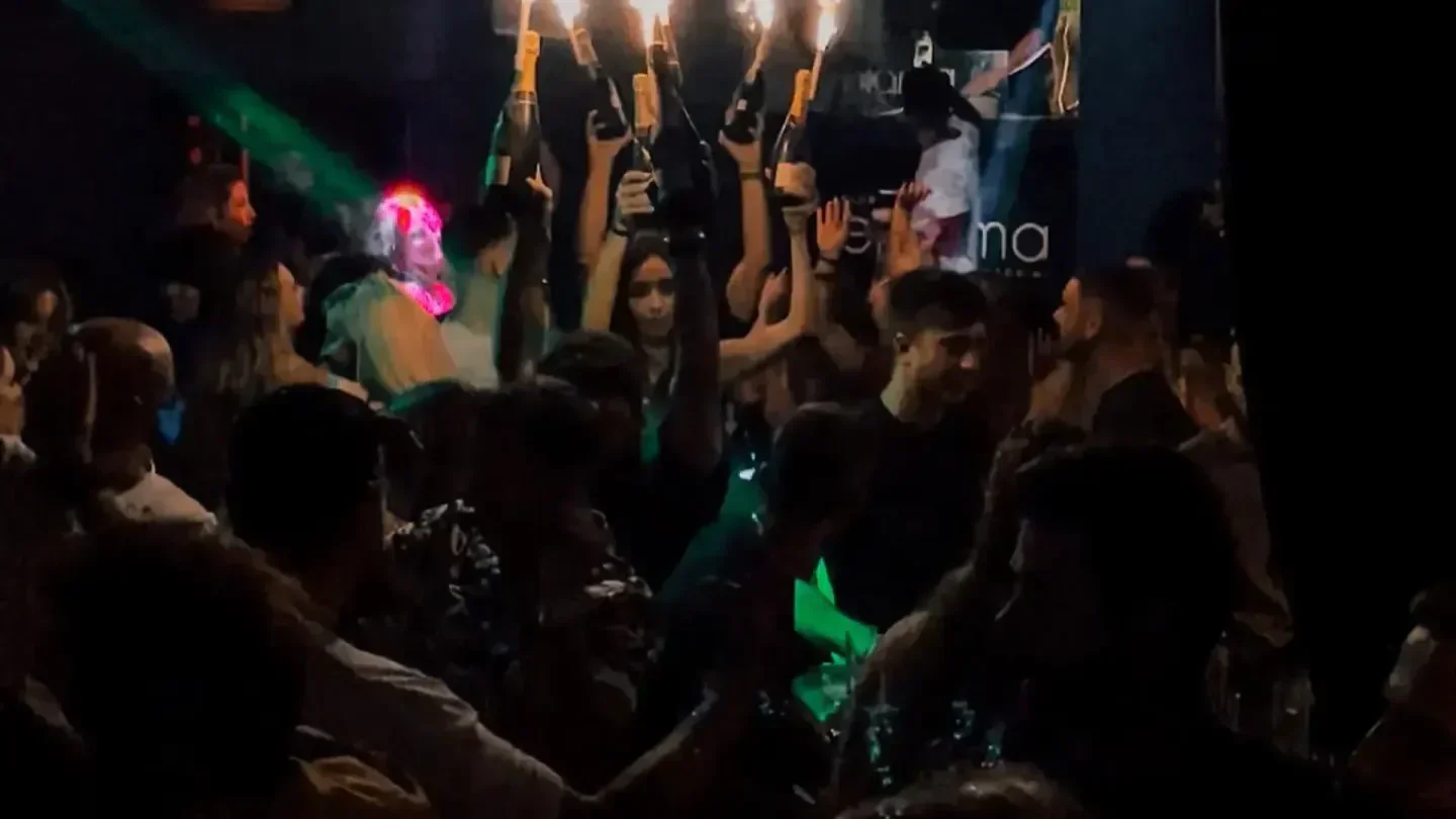 Energetic crowd celebrating at Enigma Club in Santorini with champagne bottles held high