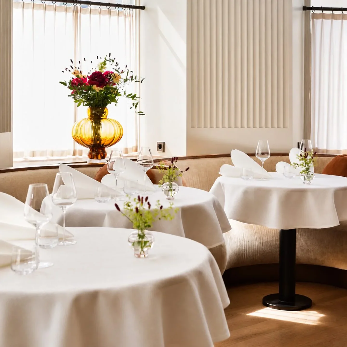 Elegant dining room at Ergo restaurant with white tablecloths, glassware, and fresh floral arrangements.