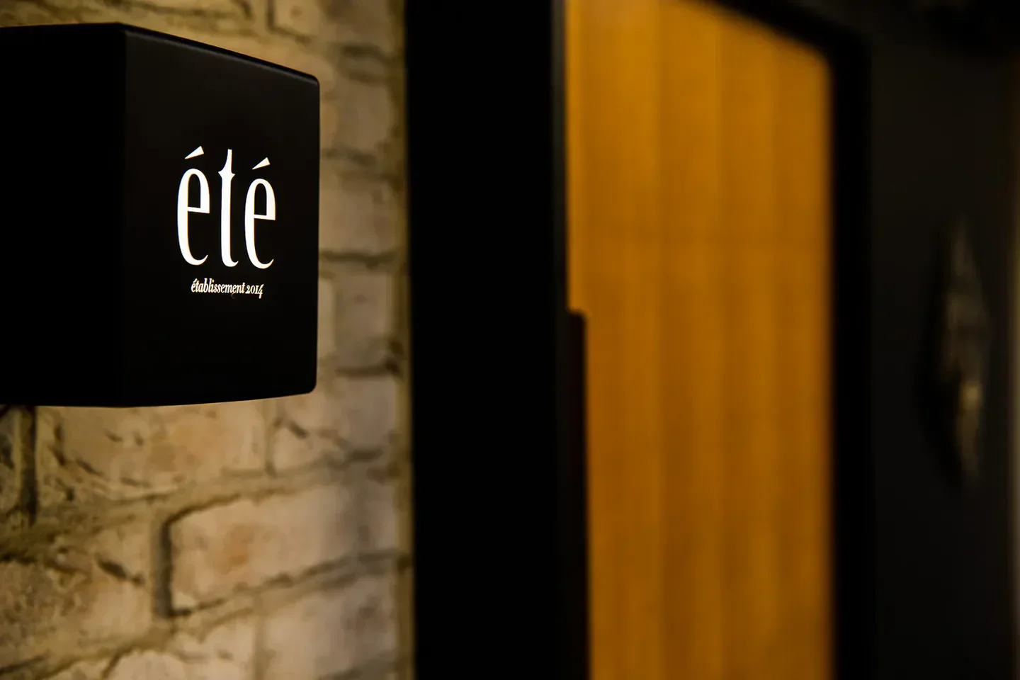 Signage of Été restaurant in Tokyo, featuring its logo on a brick wall.