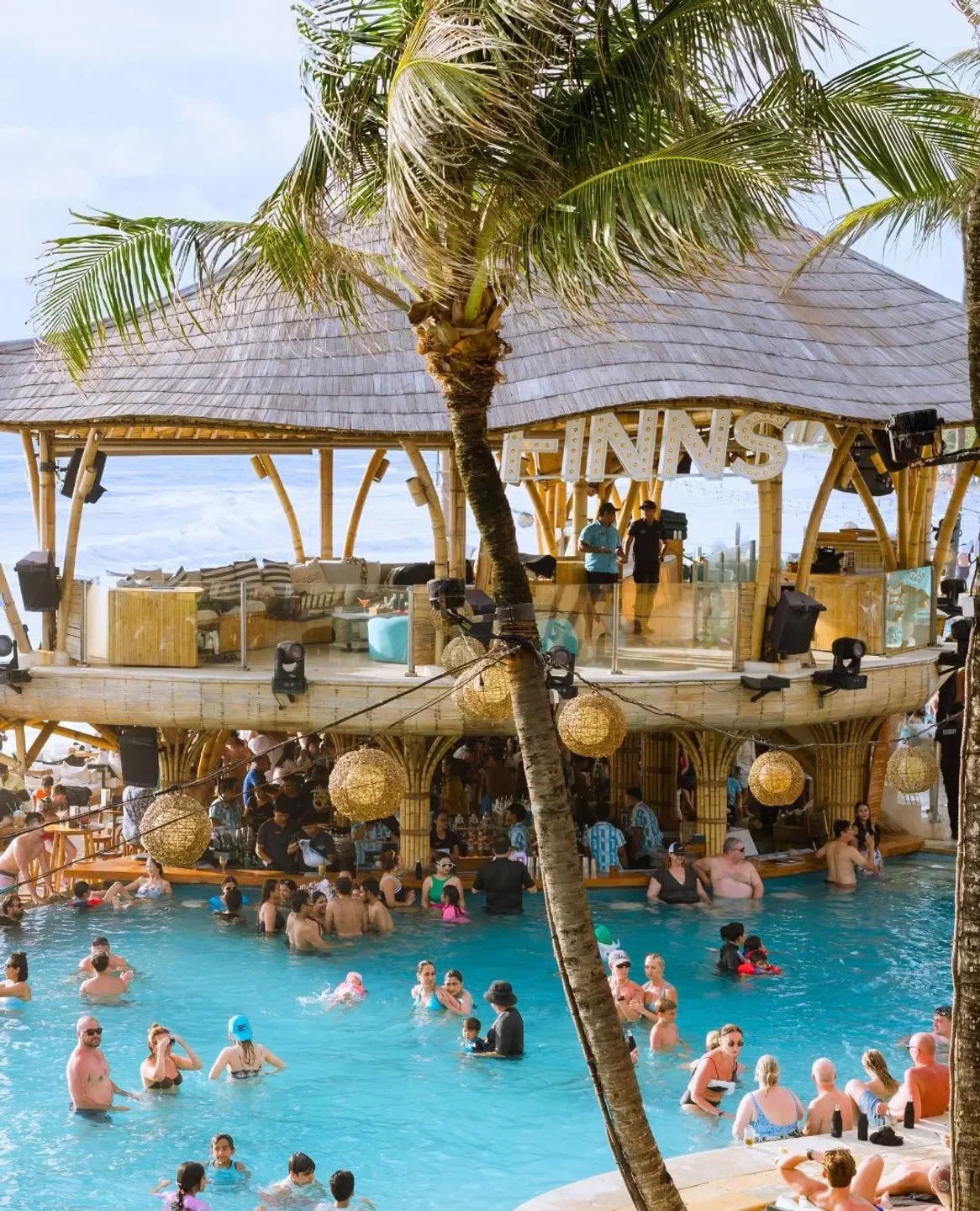 Crowd enjoying a pool at Finns Beach Club in Bali with a bar and palm trees.