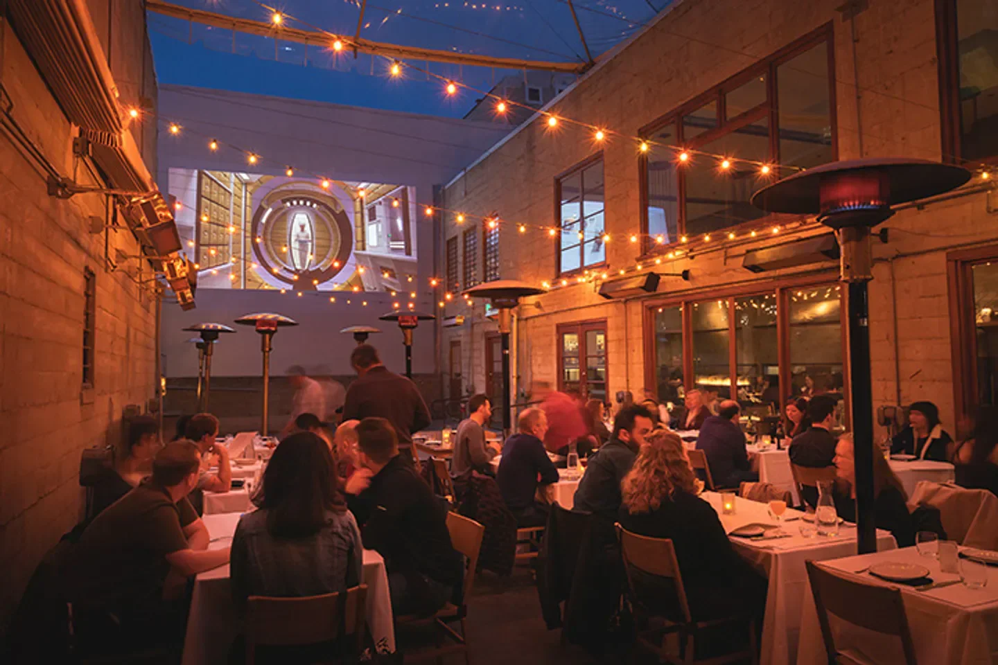 Outdoor dining at Foreign Cinema in San Francisco, with movie screen and string lights.