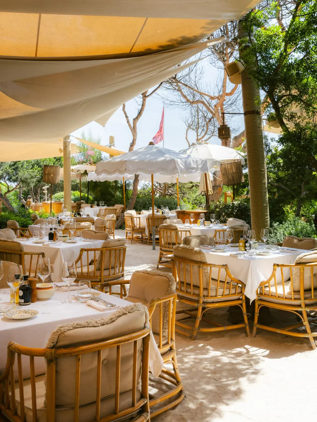 Gigi Ramatuelle Saint-Tropez outdoor seating with white tablecloths and rattan chairs under umbrellas.