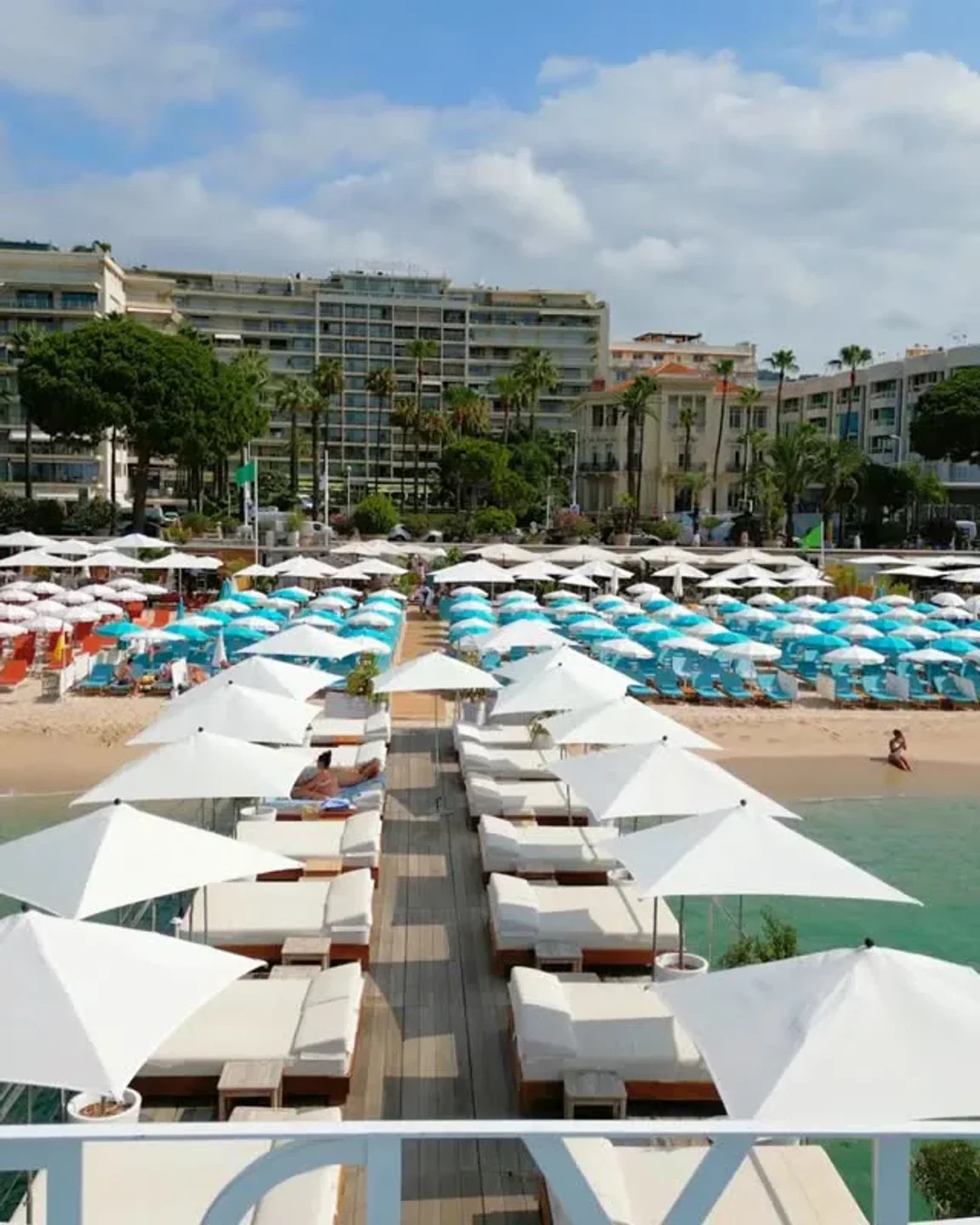 Hyde Beach Cannes offers rows of white sunbeds and umbrellas on a wooden deck overlooking the Mediterranean Sea.