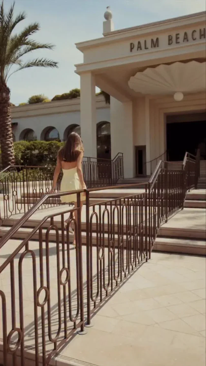 Exterior of Il Grande Palm Beach restaurant in Cannes with a woman walking up stairs on a sunny day.