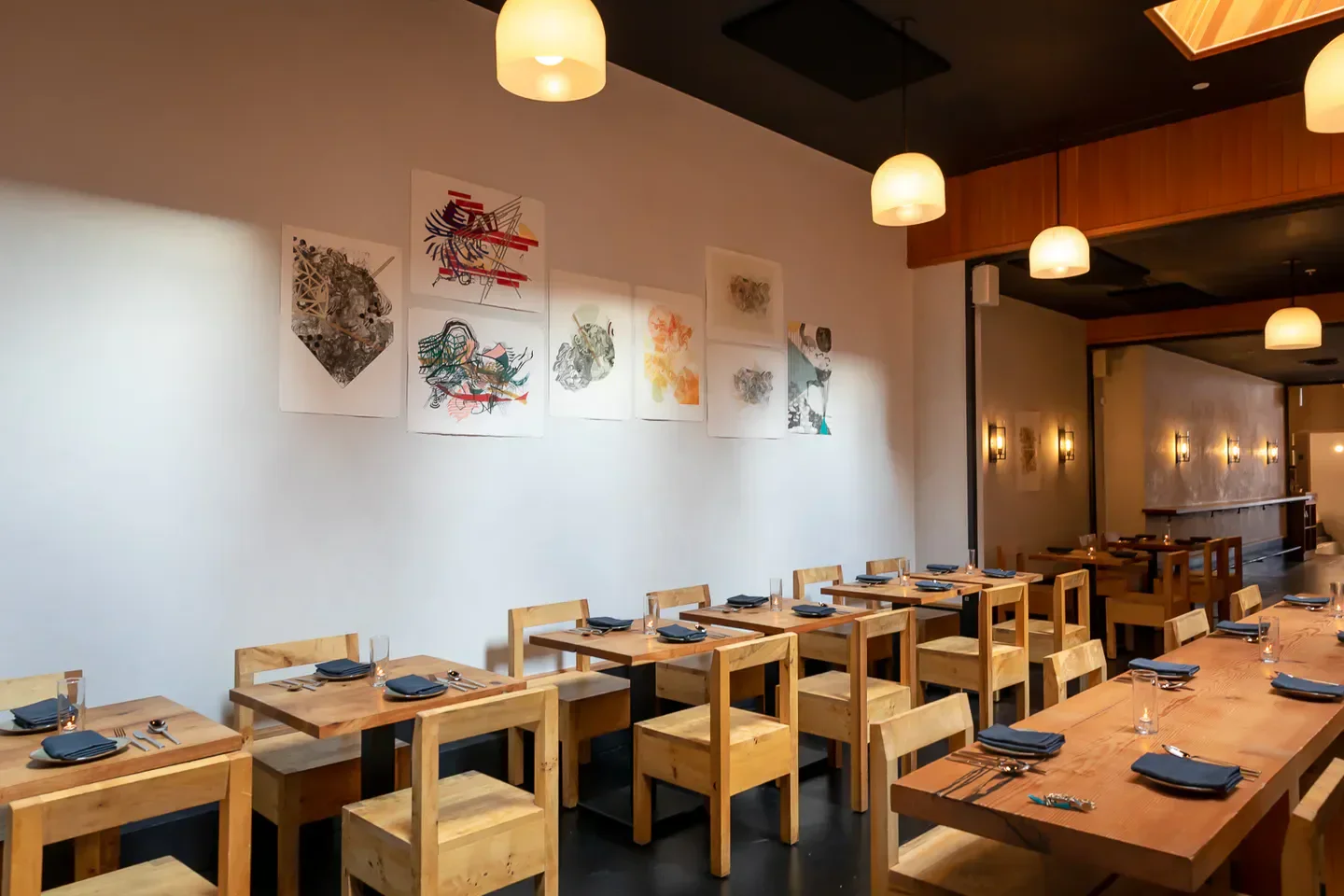 Interior dining space at Itria, a San Francisco restaurant with art and wooden tables.