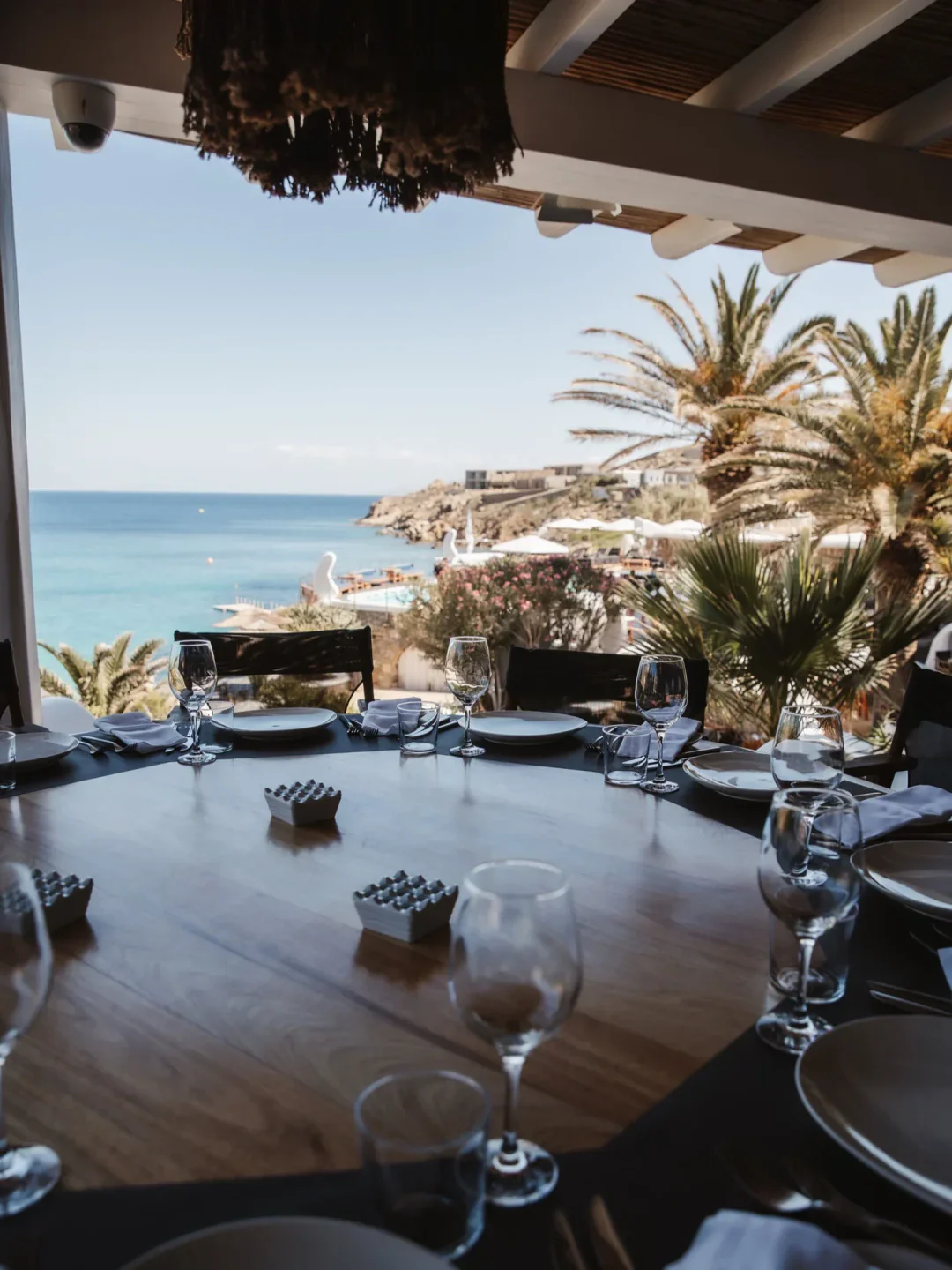 Jackie O' Town Bar in Mykonos offers stunning ocean views from a table set for dining with palm trees.