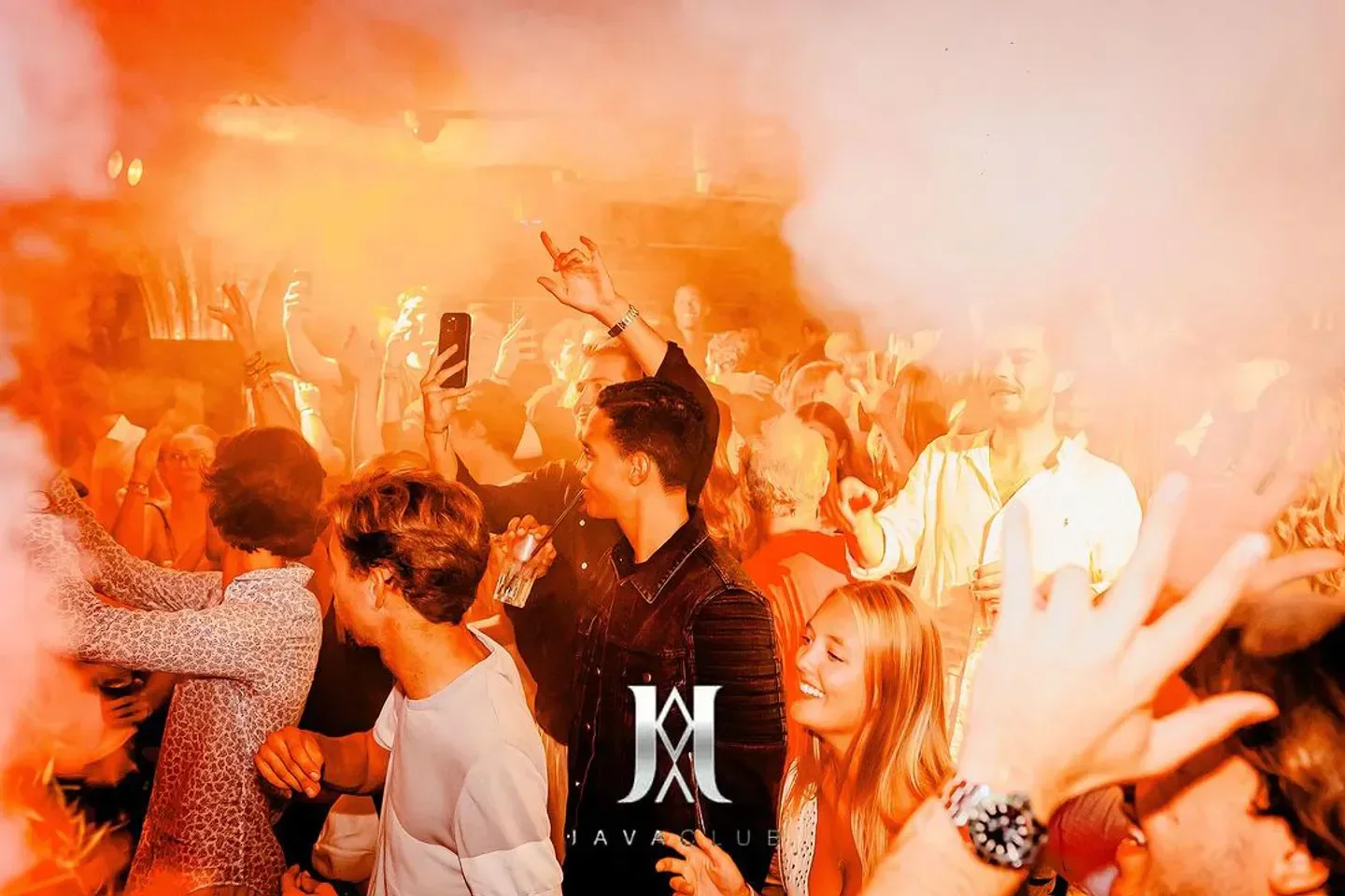 Energetic crowd partying at Java Club in Geneva, with vibrant orange lighting and smoke.
