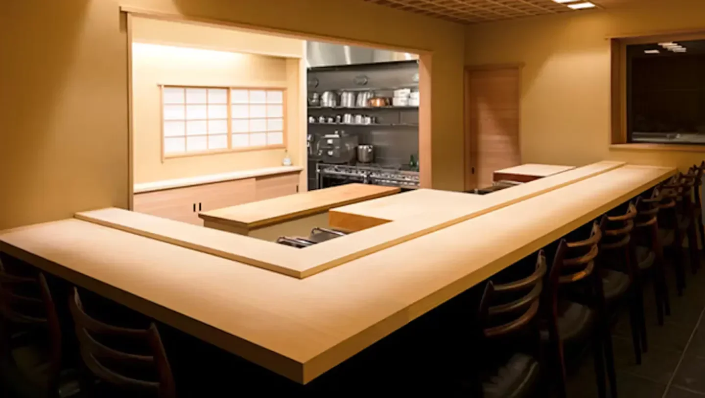 Interior of Kaiseki Komuro in Tokyo, featuring a minimalist wooden counter and kitchen.