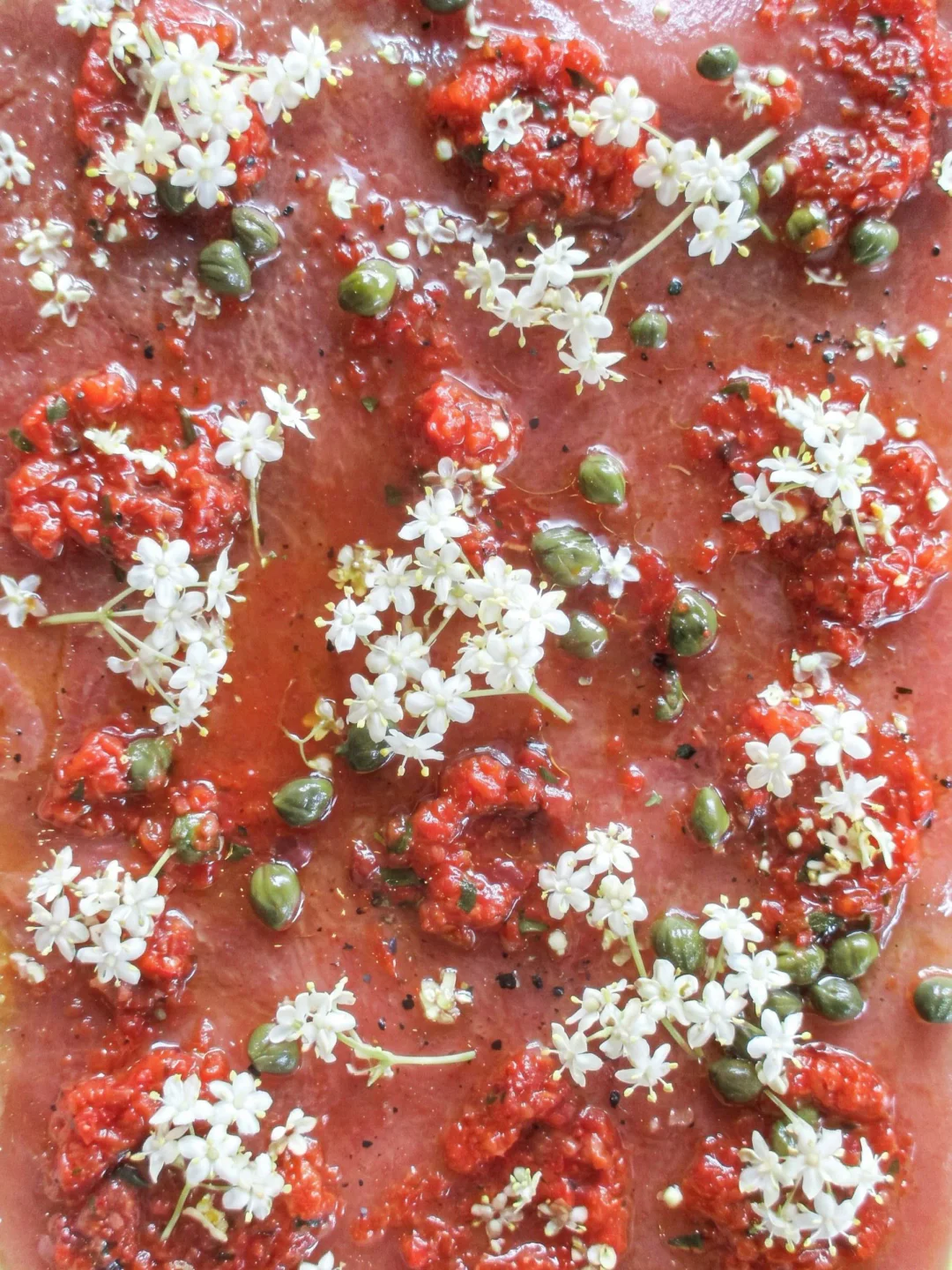 KALA Uluwatu restaurant serves a vibrant tuna carpaccio with capers, tomatoes, and delicate white flowers.