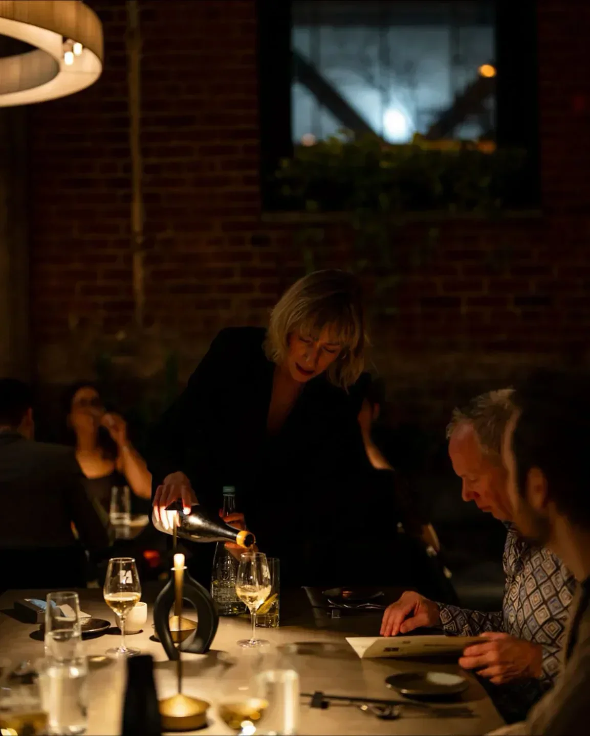 Server pouring wine at Kitano Shokudo (OTTO BISTRO) restaurant in Montreal, elegant dining scene.