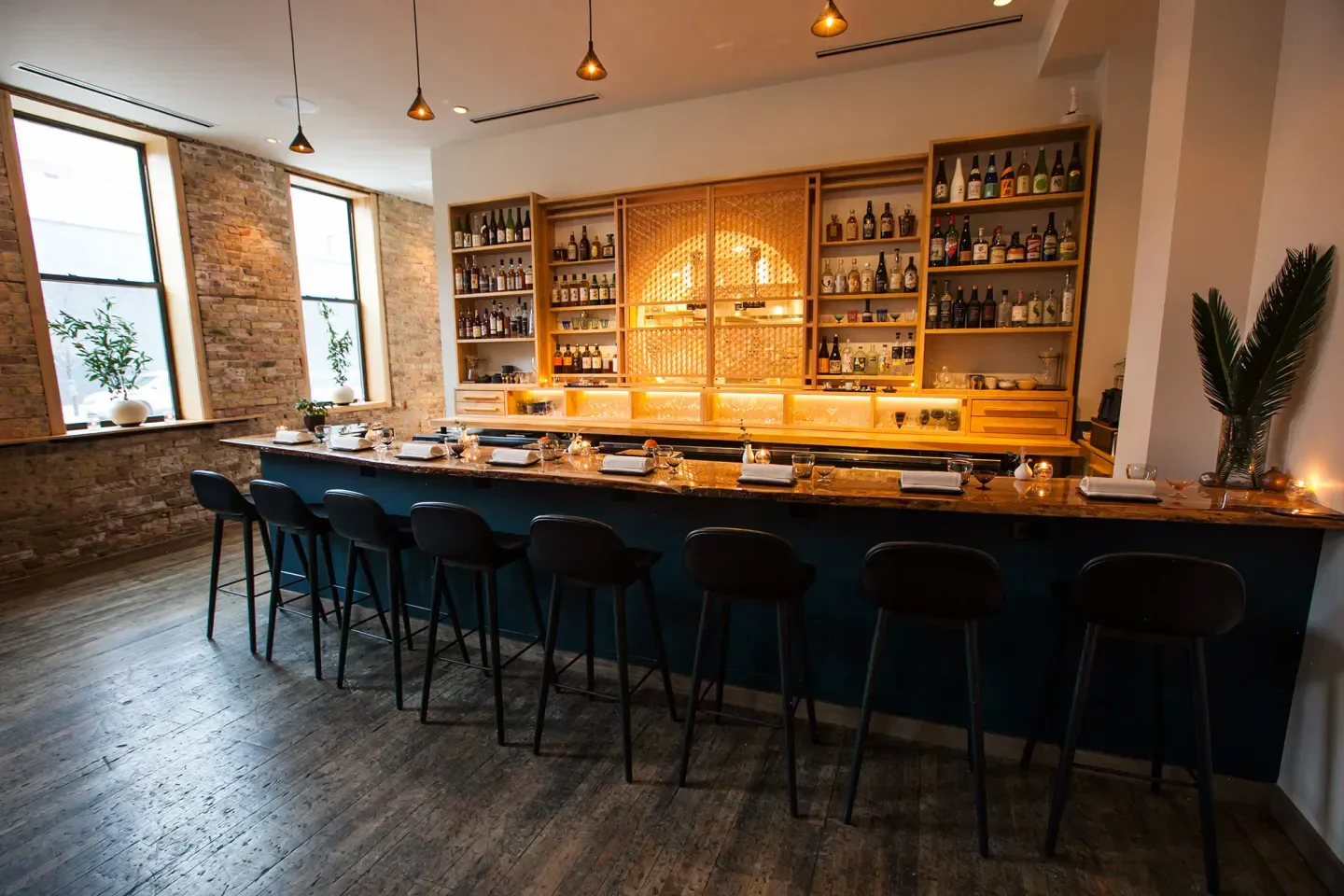 Interior of Kumiko in Chicago, showcasing the bar, chairs, and shelves of liquor bottles.