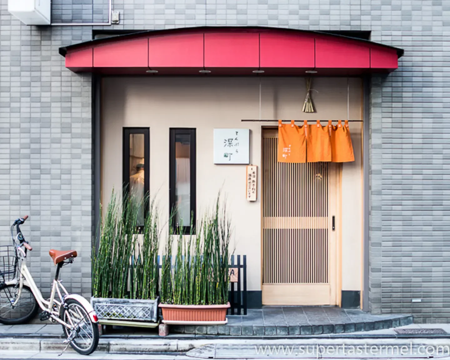 Entrance of Kyobashi Tempura Fukamachi in Tokyo, featuring traditional Japanese design and a bicycle.