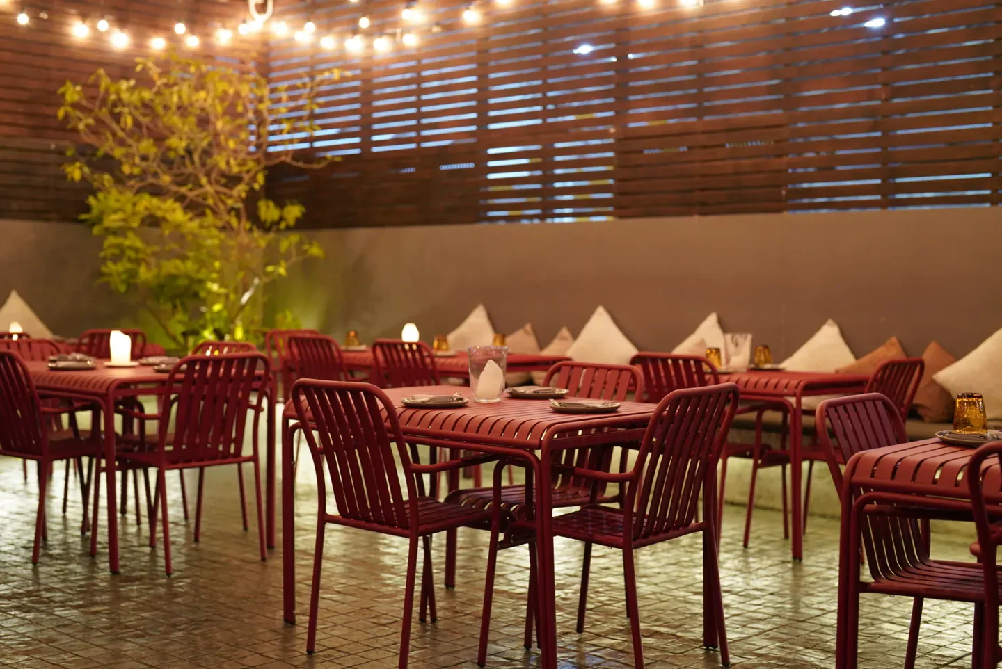 Outdoor dining area at La Casa Nostra restaurant in Bangkok with warm lighting and red furniture.