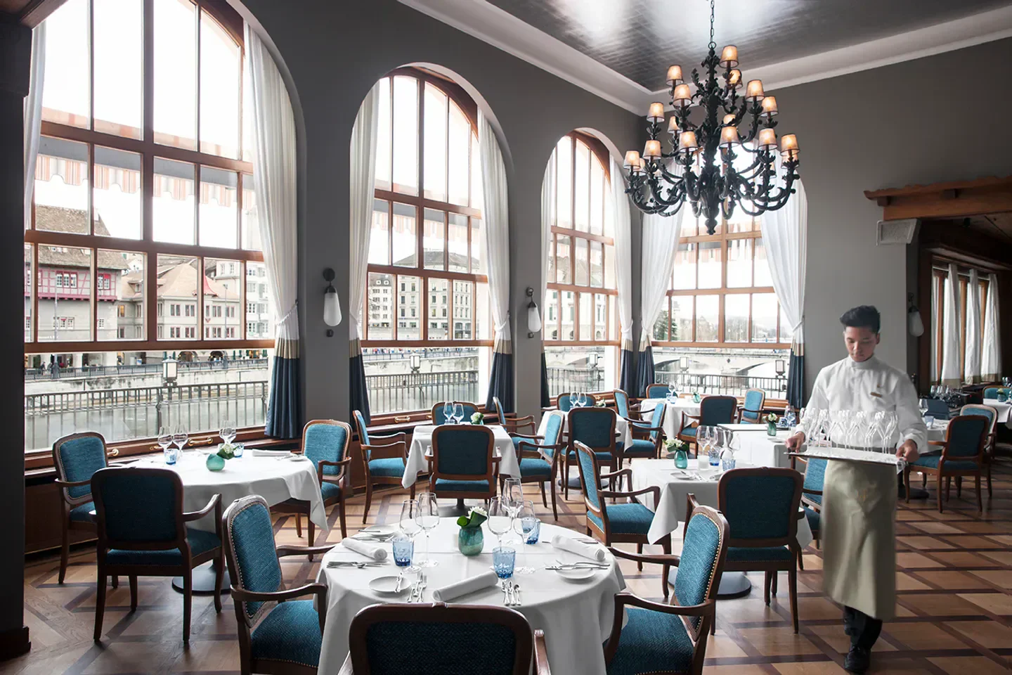 Elegant dining room at La Rôtisserie in Zurich, with city views and waiter service.