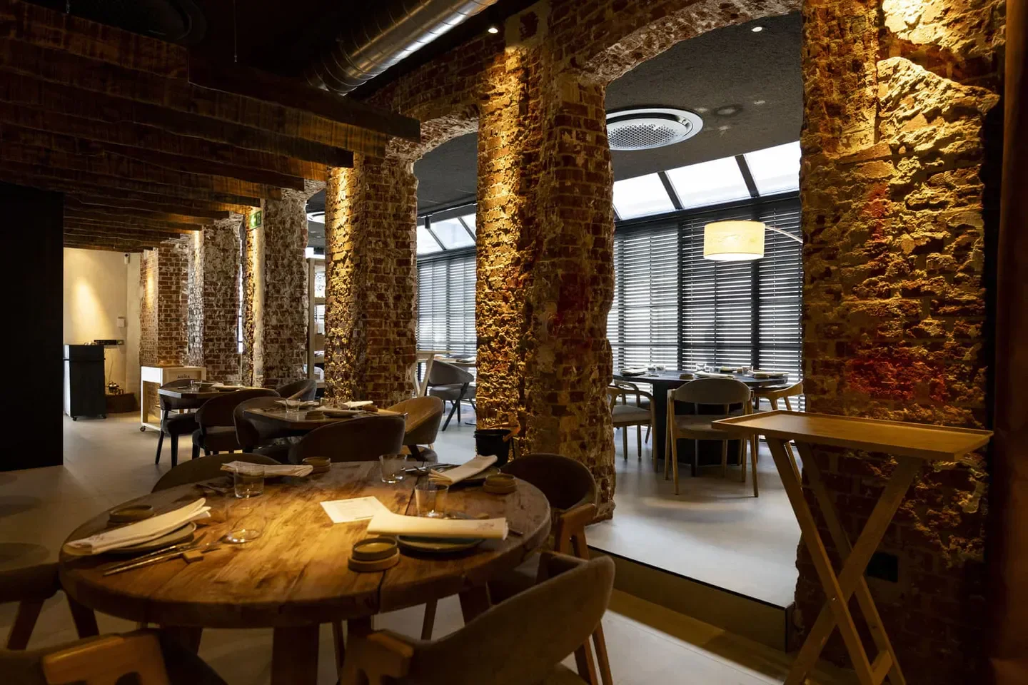 Interior of La Tasquería restaurant in Madrid, featuring rustic brick pillars and wooden tables.