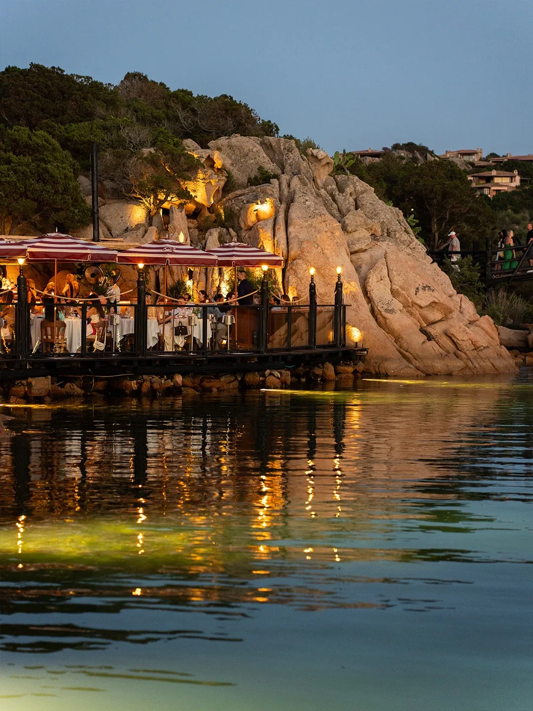 Langosteria restaurant exterior with striped umbrellas and illuminated tables overlooking the water in Porto Cervo.
