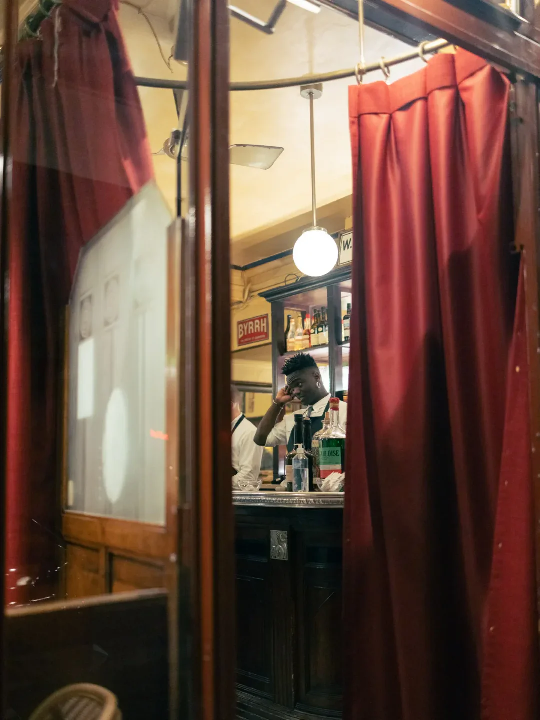 Le Bistrot Paul Bert bar interior in Paris with red velvet curtains and a bartender