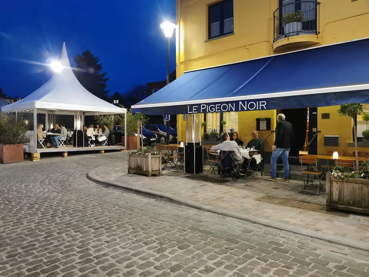 Outdoor seating at Le Pigeon Noir restaurant in Brussels, with a white tent at night