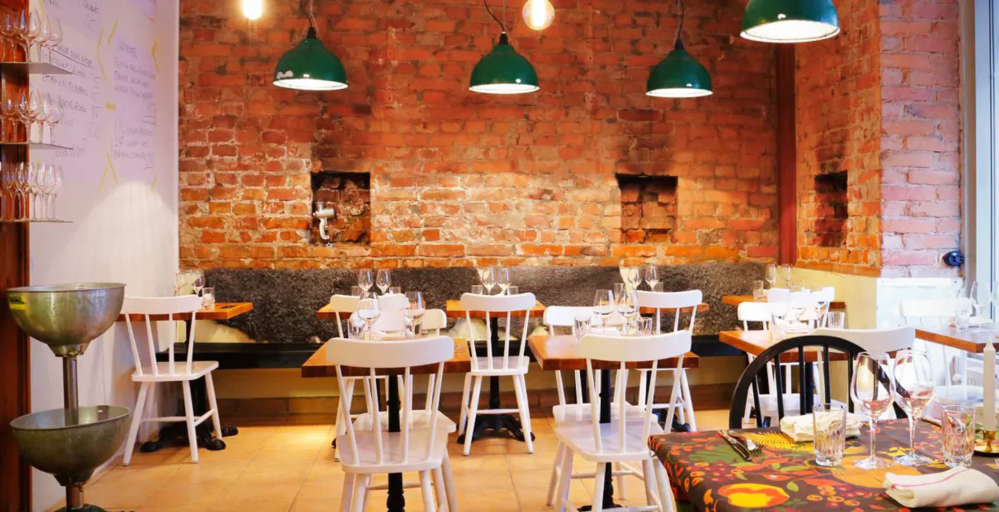 Cozy dining room at Lilla Ego restaurant in Stockholm with exposed brick and white chairs.