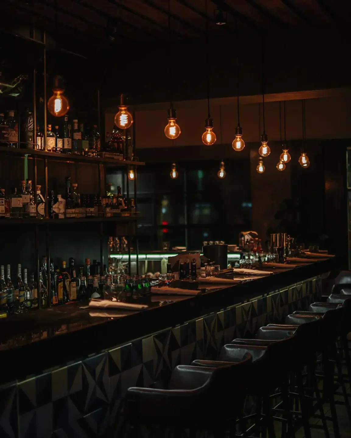 Cozy bar interior at Longtail Taipei, featuring hanging lights and well-stocked shelves.