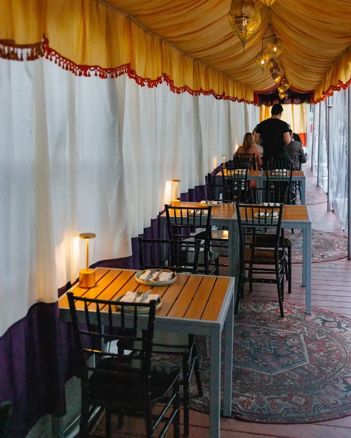 Cozy dining area at Maydān restaurant in Washington, with tables set and hanging lanterns.