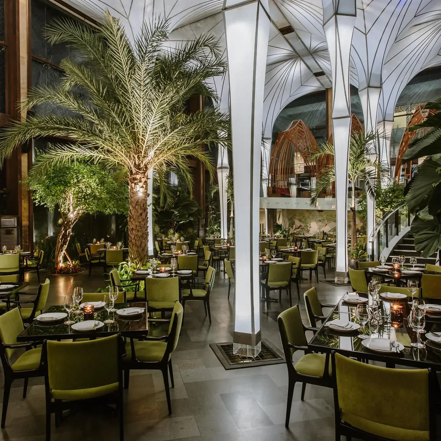 Interior of Merah Putih restaurant in Bali, with palm trees and elegant dining tables.