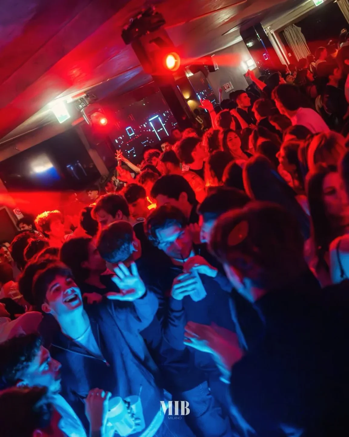 Energetic crowd dancing under red and blue lights at MiB Milano nightclub in the city.