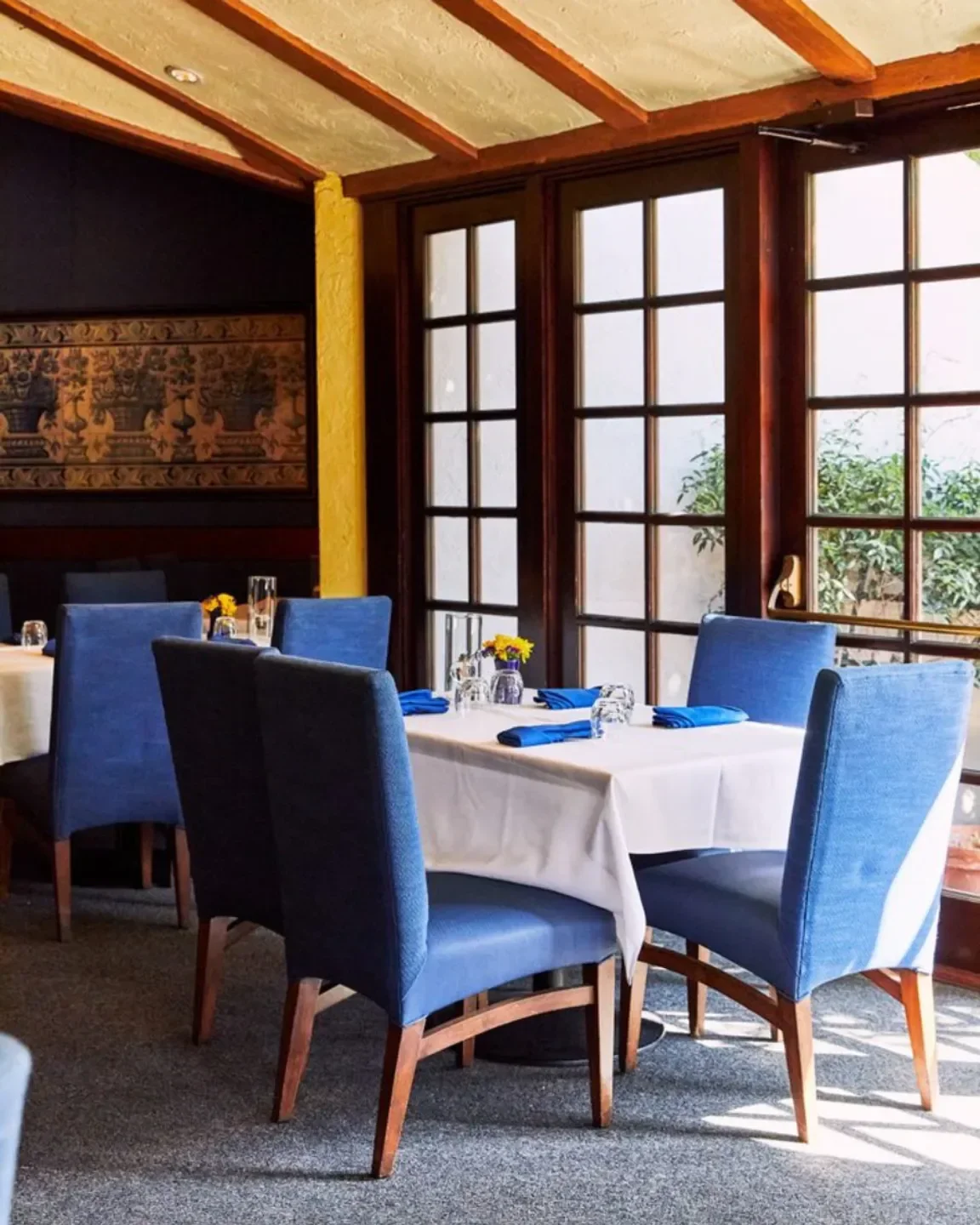 Dining area at Mille Fleurs restaurant in San Diego with blue chairs and white tablecloths.